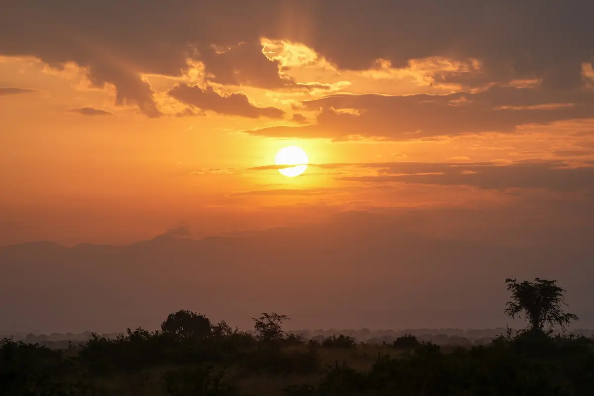 The sun rising orange over the savanna and hills of western Uganda